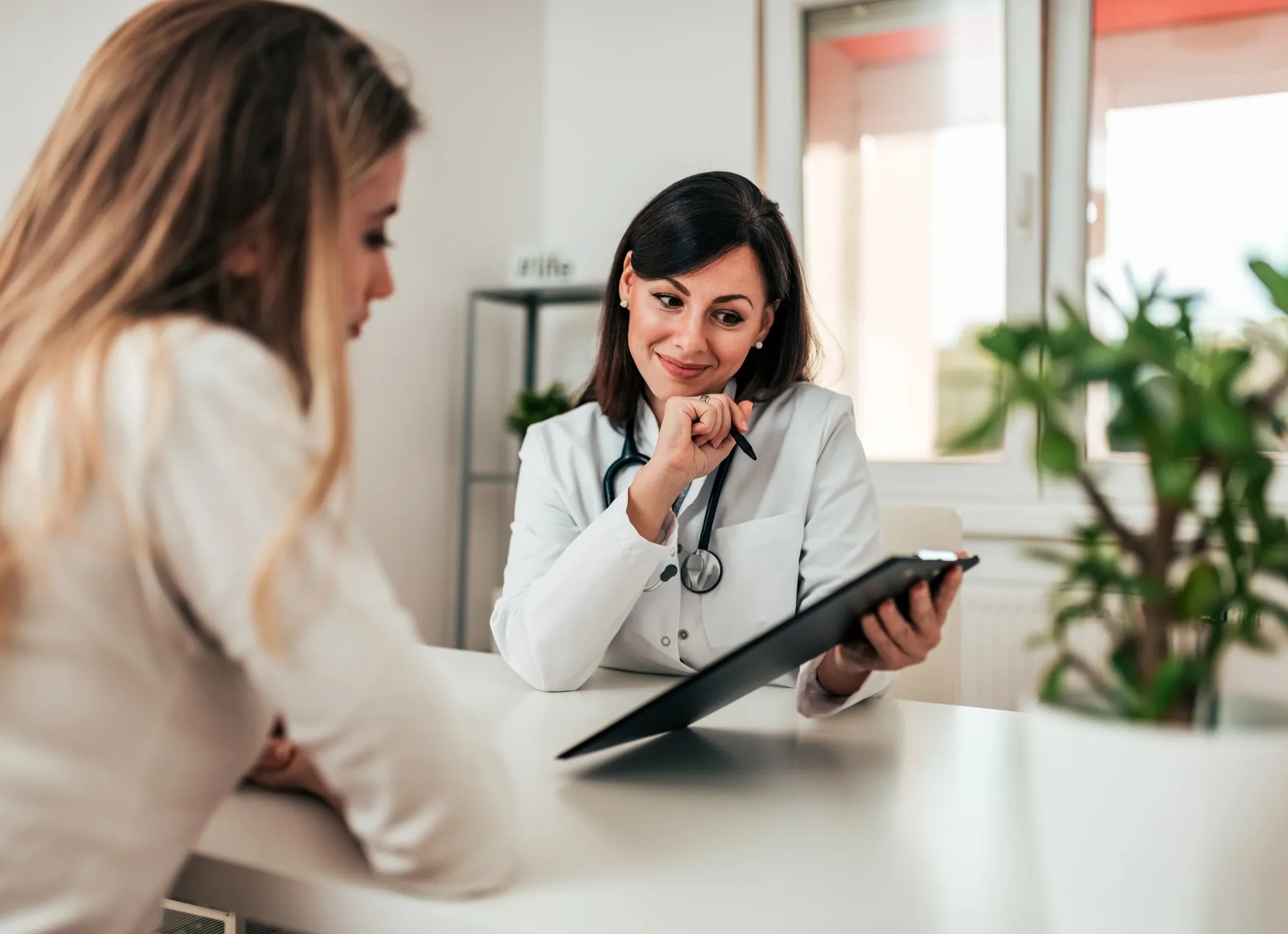 A physician sitting with a patient at a bright consulting-room desk, going through notes together.