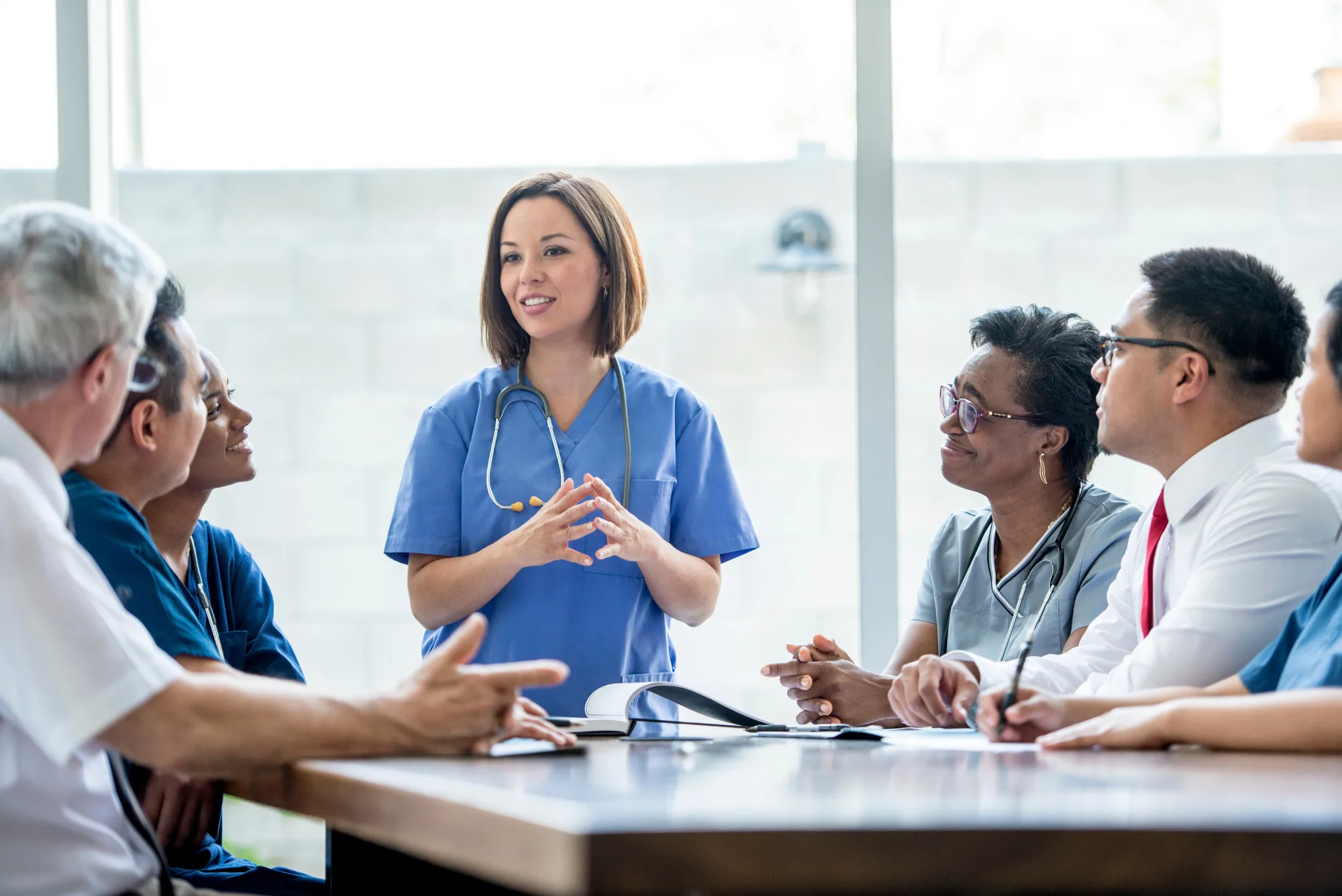 A physician leads a seated care team through a planning discussion around a conference table, illustrating how to scale a concierge practice without losing its culture.