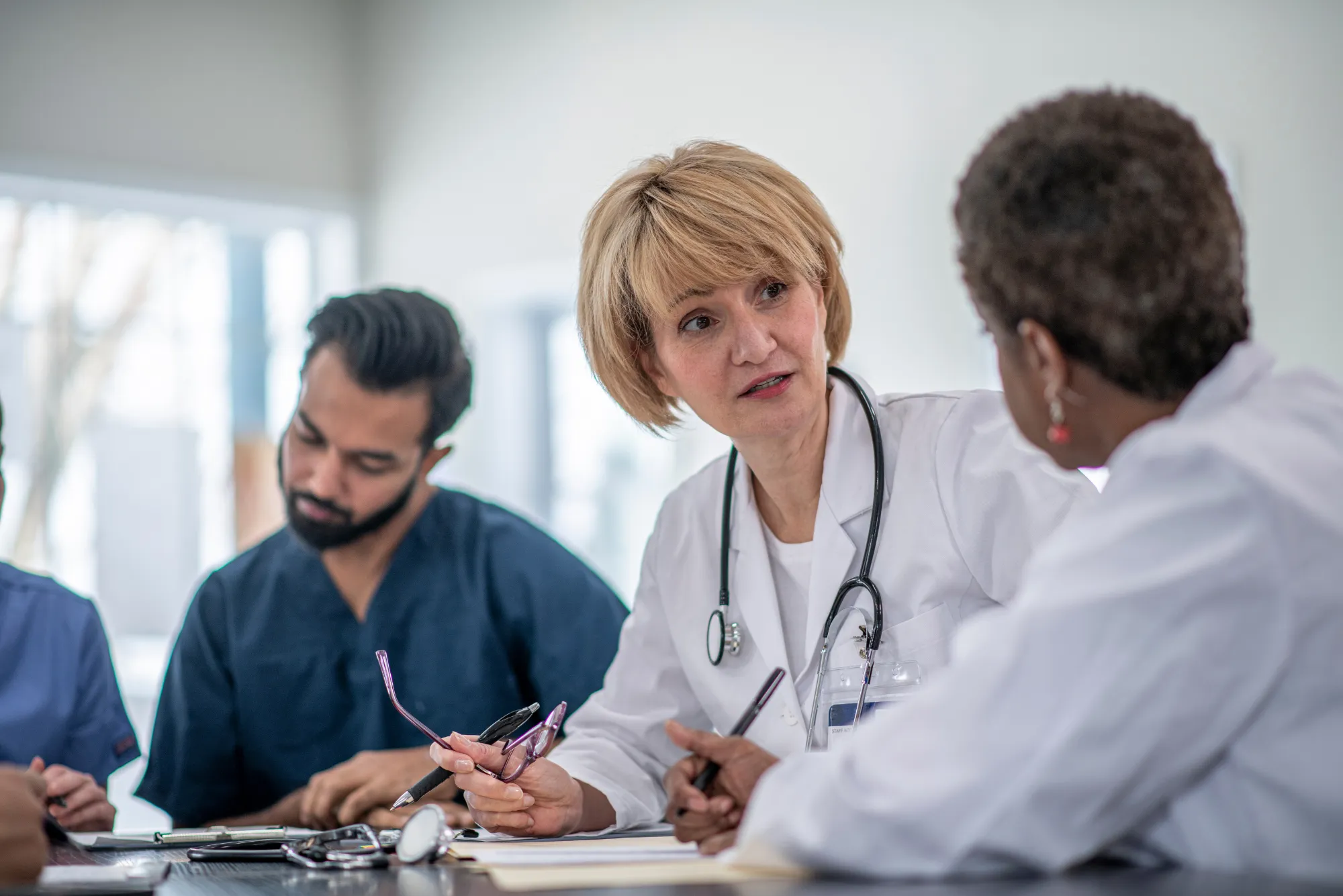 Two physicians in white coats discuss key person disability insurance at a table with a colleague nearby.