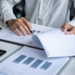 Professional reviewing financial spreadsheets and bar charts with a calculator and pen at a desk.