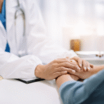 A doctor’s hands gently holding a patient’s hands in a gesture of care and comfort.