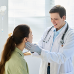 Physician in white coat examines patient in bright clinic setting.